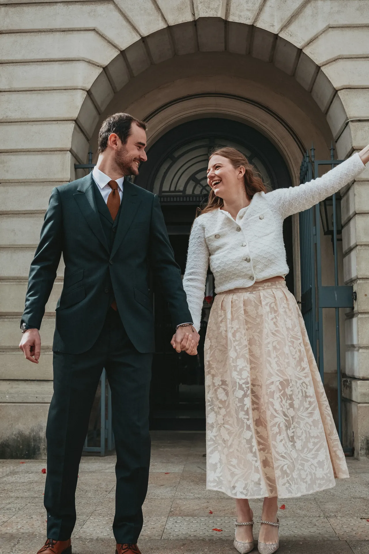 Un marié et une mariée en tenue de mariage sortent de la mairie heureux durant leur mariage civil.